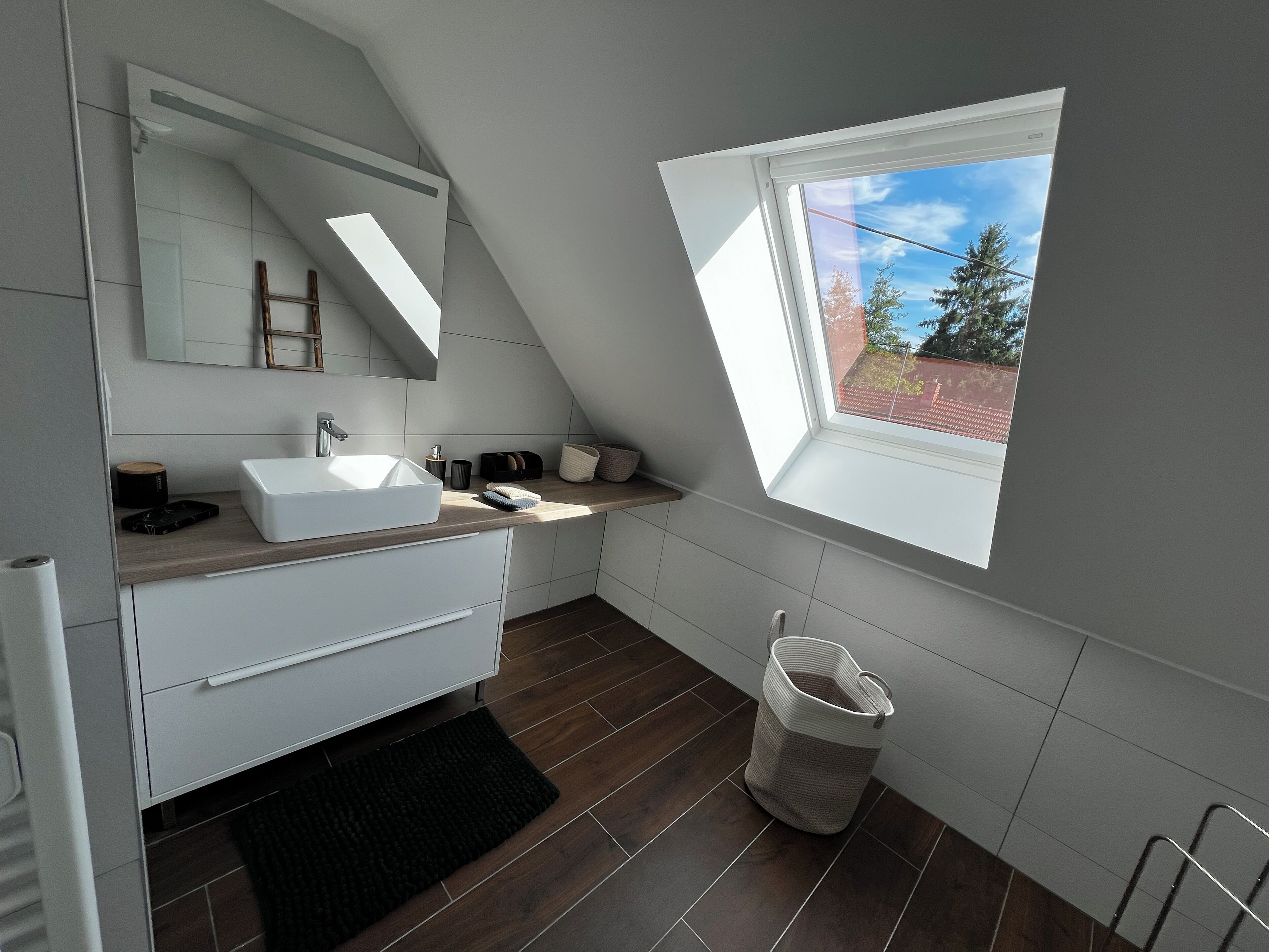 A modern bathroom with a skylight, a large mirror, and a white sink.