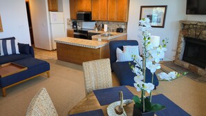 A modern living room with a sofa, a dining table with a vase of orchids, a kitchen area with wooden cabinets, and a stone fireplace. - Tahoe Vista Inn Suite 2 (Tahoe Vista)