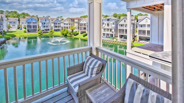 A balcony with wicker furniture overlooking a lake and residential buildings. - 42 Sandcastle | Free Heated Pool | 3 Blocks to the Beach | Elevator (Hilton Head Island)