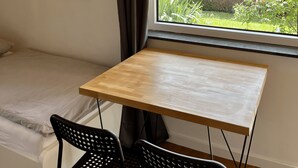 A room with a bed, a table, and a window with a view of a garden and houses. - Schwabenperle Apartments  (Laucheim)