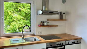 A modern kitchen with a stainless steel range hood, a built-in oven, and a window overlooking greenery. - Schwabenperle Apartments  (Laucheim)