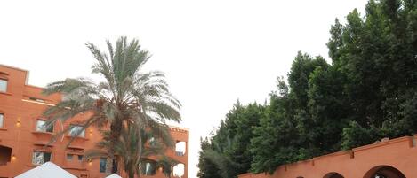 A swimming pool with lounge chairs and umbrellas, surrounded by a building with arches and palm trees.