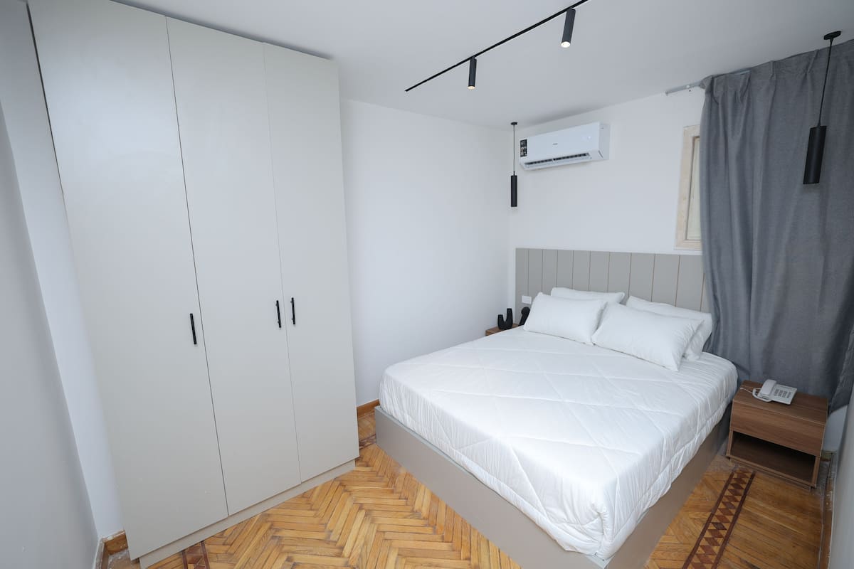 A bedroom with a bed, wardrobe, bedside table, and a hanging light fixture.