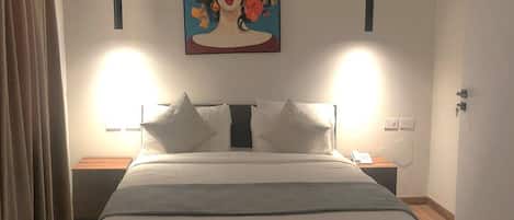 A bedroom with a bed, two bedside tables, a painting on the wall, and a ceiling light fixture.