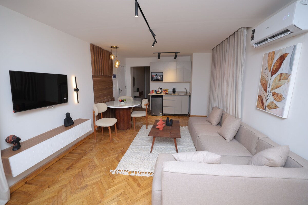 A modern living room with a sofa, coffee table, TV, and a dining area with chairs and a table.