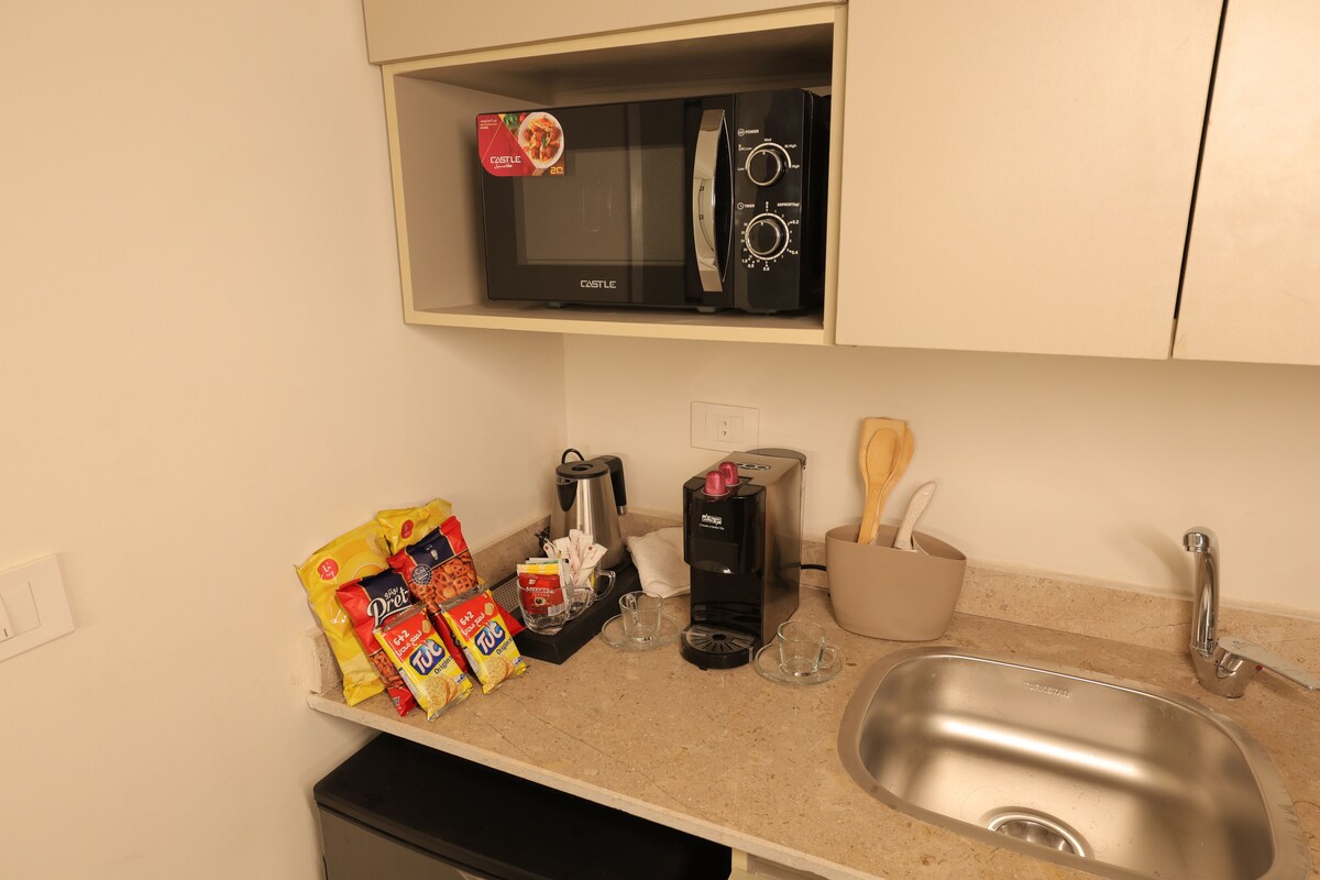 A kitchen with a microwave, coffee maker, and a sink. There are snacks and a coffee pot on the counter.