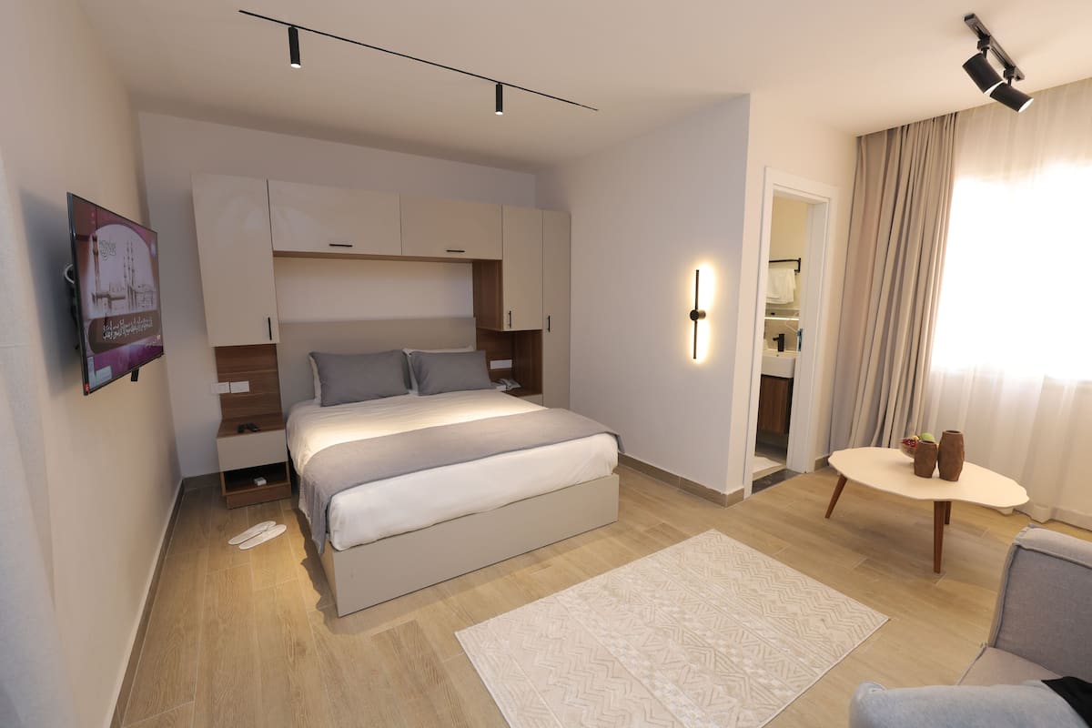 A modern hotel room with a large bed, bedside tables, a small round table, and a view of the bathroom.