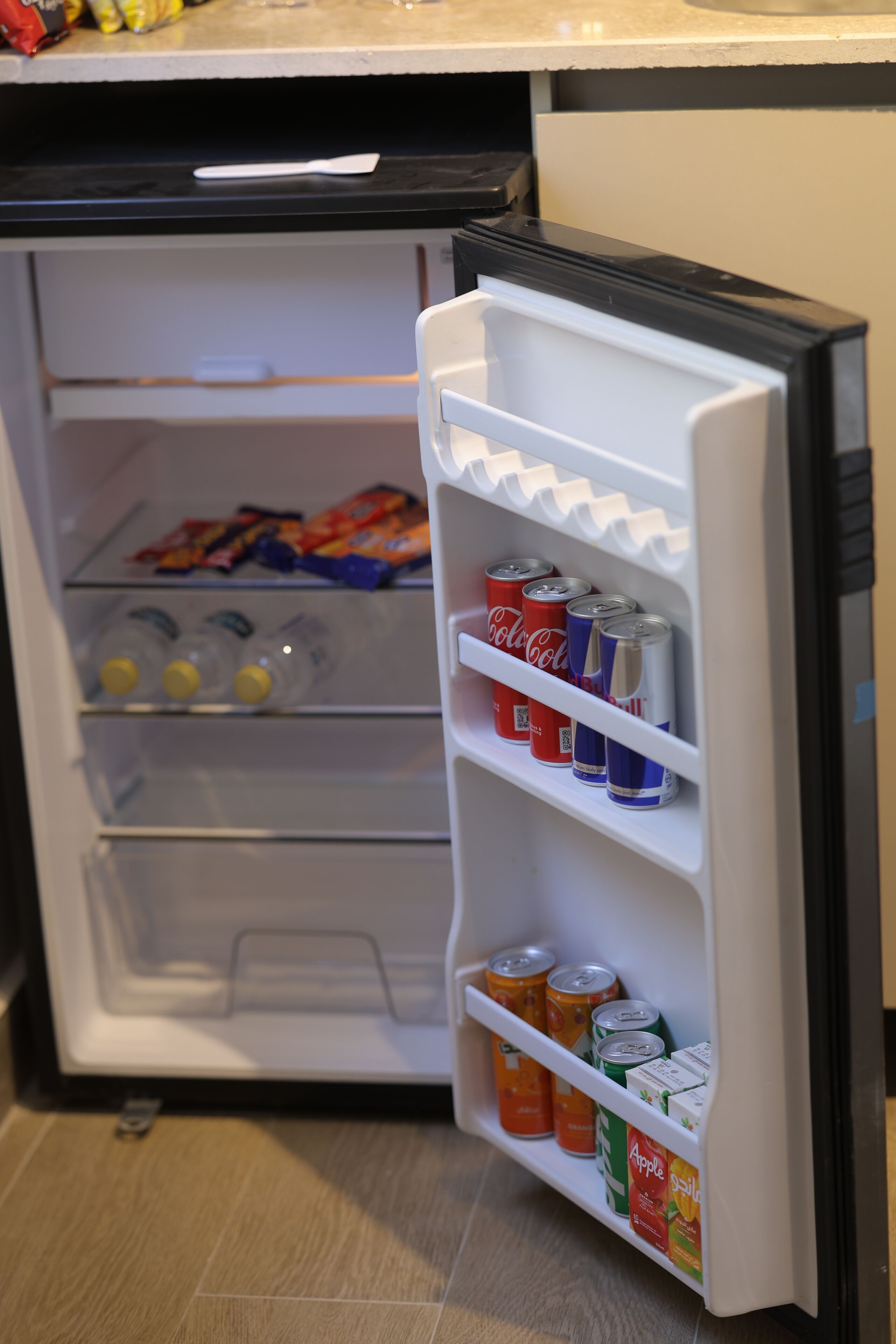 A compact refrigerator with shelves containing beverages and snacks.