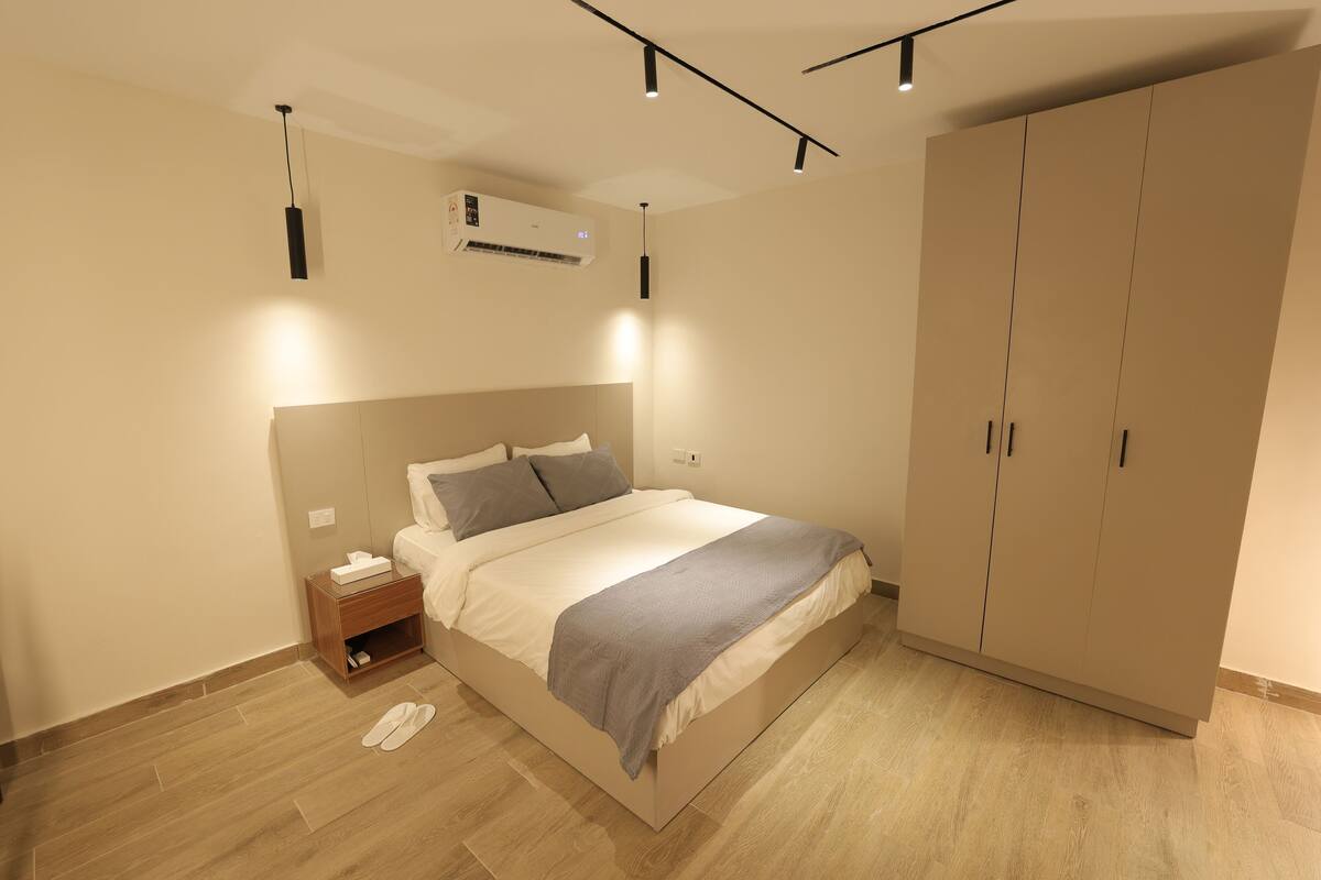 A bedroom with a bed, bedside table, nightstand, wardrobe, and ceiling lights.