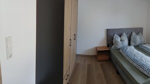 A small bedroom with a bed, a nightstand, a window, and a wooden wardrobe. - Modern vacation apartment in Kehl, 60m2 comfort on one level (Weißenburg in Bayern)
