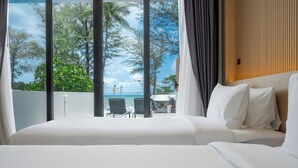 Habitación de hotel con una cama grande, vista a la playa y un balcón con sillas.