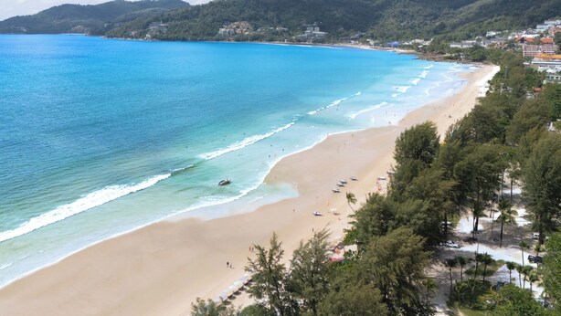 Una playa con agua azul cristalina, orilla de arena y un promontorio boscoso al fondo.