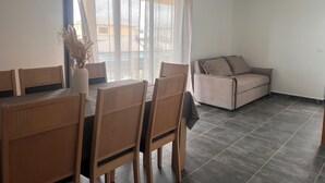 Zona de menjador amb taula i cadires, un sofà i vista a través de cortines translúcides.