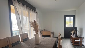 Habitació amb taula de dinar preparada per a dues persones, un ram de flors seques, un llit amb capçalera de fusta i un televisor sobre un suport de fusta.