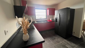 Una cuina petita amb taulell negre, armaris vermells, nevera d'acer inoxidable i una finestra que deixa entrar llum natural.