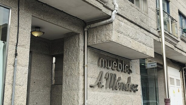 Um edifício com fachada de pedra, um letreiro com a inscrição "muebles A.M." e um carro estacionado em frente.
