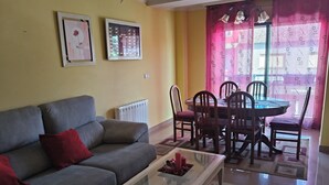 Uma sala de estar com um sofá cinzento, uma mesa de centro de vidro e um espaço de jantar com mesa e cadeiras.