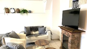 A living room with a white sofa, two armchairs, a coffee table, a fireplace, and a television. - Mi Casita: 1-room apartment with three single beds, 2min to the highway (Florstadt)