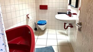 A small bathroom with a red bathtub, a white sink, a blue toilet, and a red towel rack. - Mi Casita: 1-room apartment with three single beds, 2min to the highway (Florstadt)