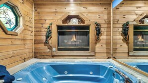 Interior de una cabaña de madera con un jacuzzi, chimenea y una ventana de vitral.
