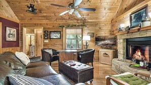 Interior acogedor de una cabaña con chimenea, muebles de cuero y un televisor montado en la pared.