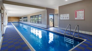 Una piscina interior con agua azul cristalina, suelo de baldosas y un cartel que indica 'RAMADA' en la pared.
