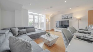Ein modernes Wohnzimmer mit einem grauen Ecksofa, einem Marmortisch und einem Essbereich mit Tisch für zwei Personen.