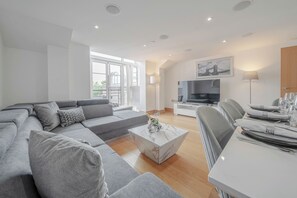 Una sala de estar moderna con un sofá seccional gris, una mesa de centro de mármol y una zona de comedor con una mesa preparada para dos.