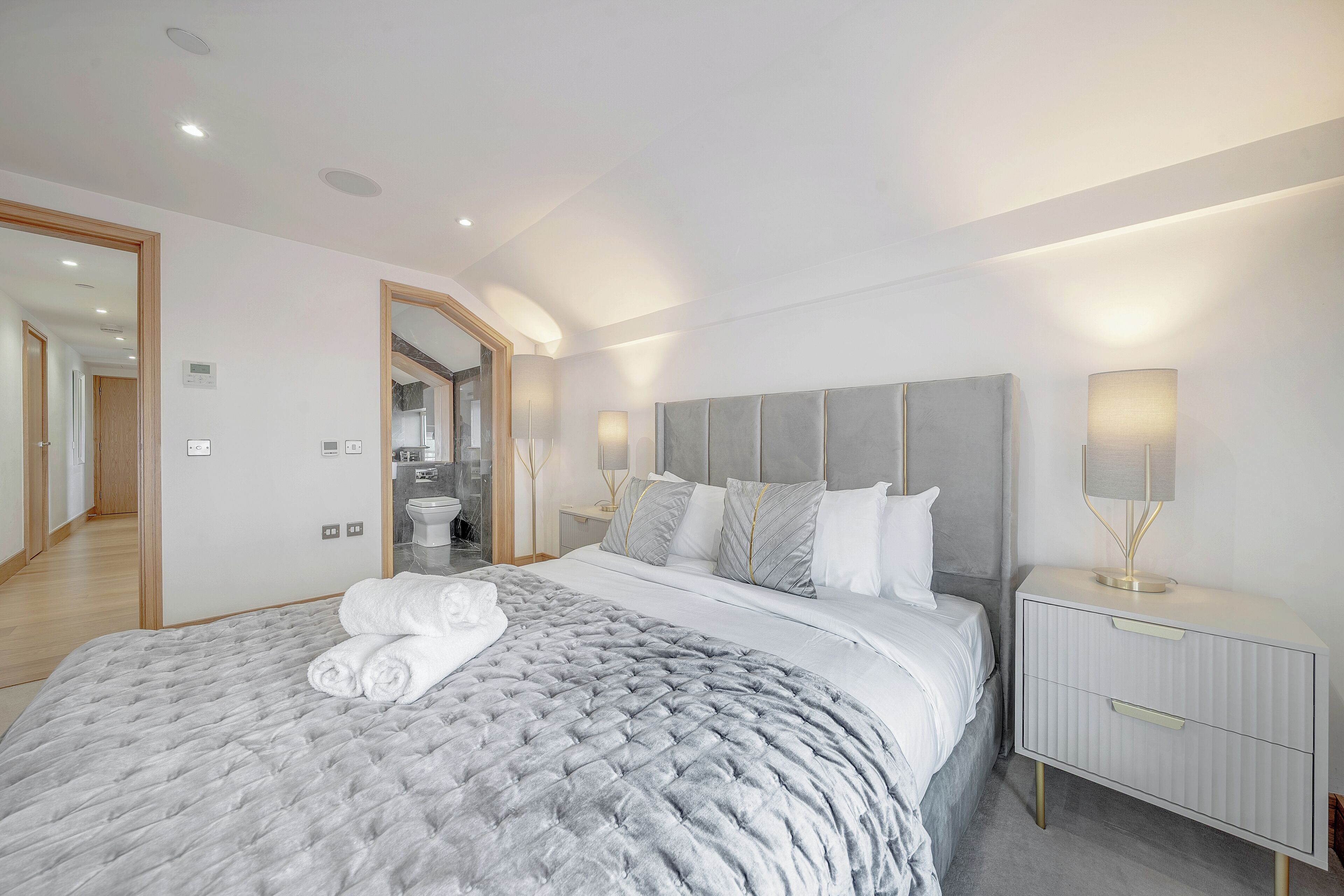 A modern bedroom with a large bed, a nightstand, and a bathroom visible through an open door.