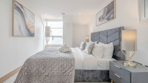 Ein modernes Schlafzimmer mit einem großen Bett, einem Nachttisch mit Lampe und Kunstwerken an den Wänden.