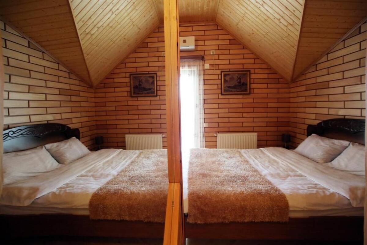Quarto com espelhos, duas camas, paredes de madeira e teto inclinado.