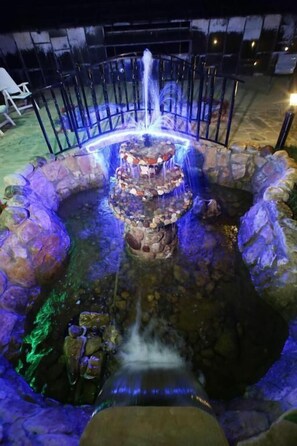 A nighttime outdoor water feature with a central fountain surrounded by rocks and illuminated by blue lighting. - Hotel Harmony (Tsqaltubo)