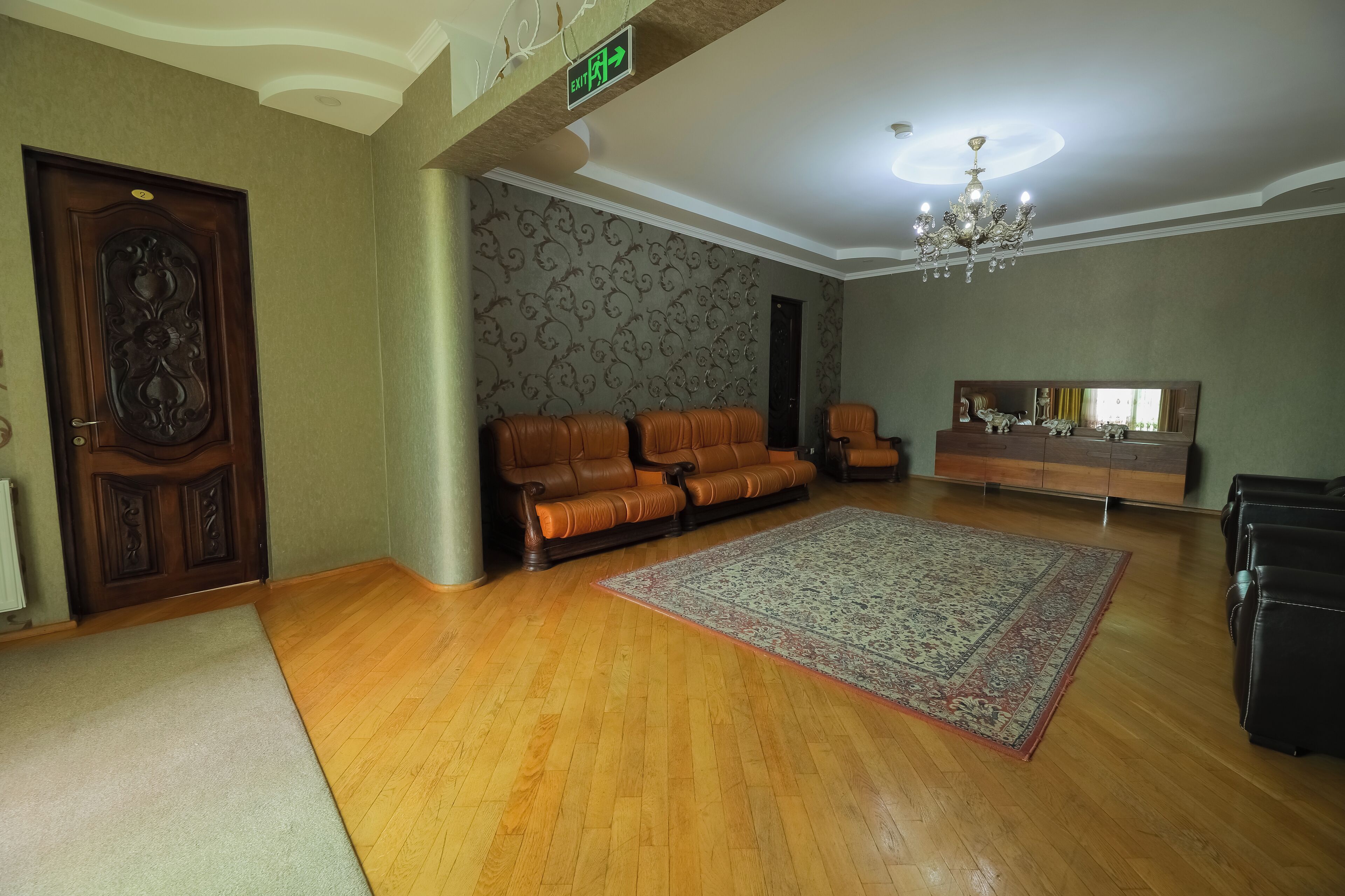 A spacious living room with a wooden floor, leather sofas, a large rug, and a chandelier.
