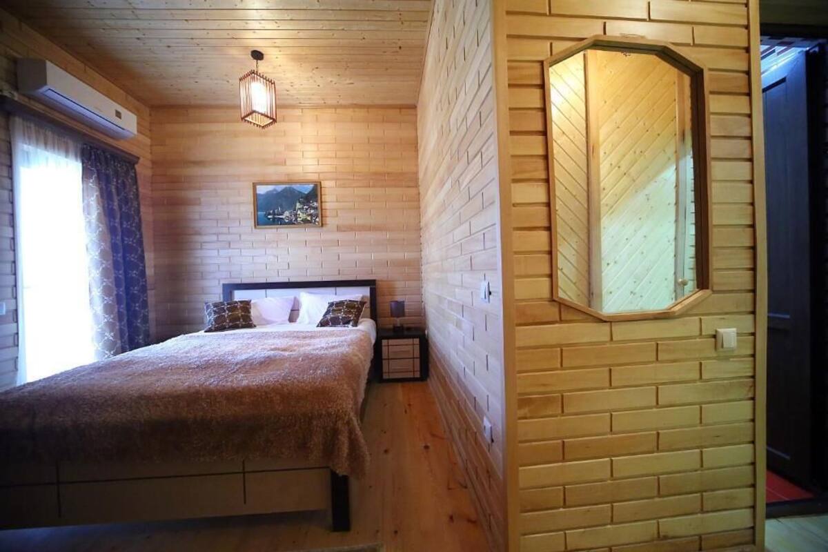 Quarto com painéis de madeira, uma cama, uma mesinha de cabeceira, um espelho fixado na parede e uma pintura.