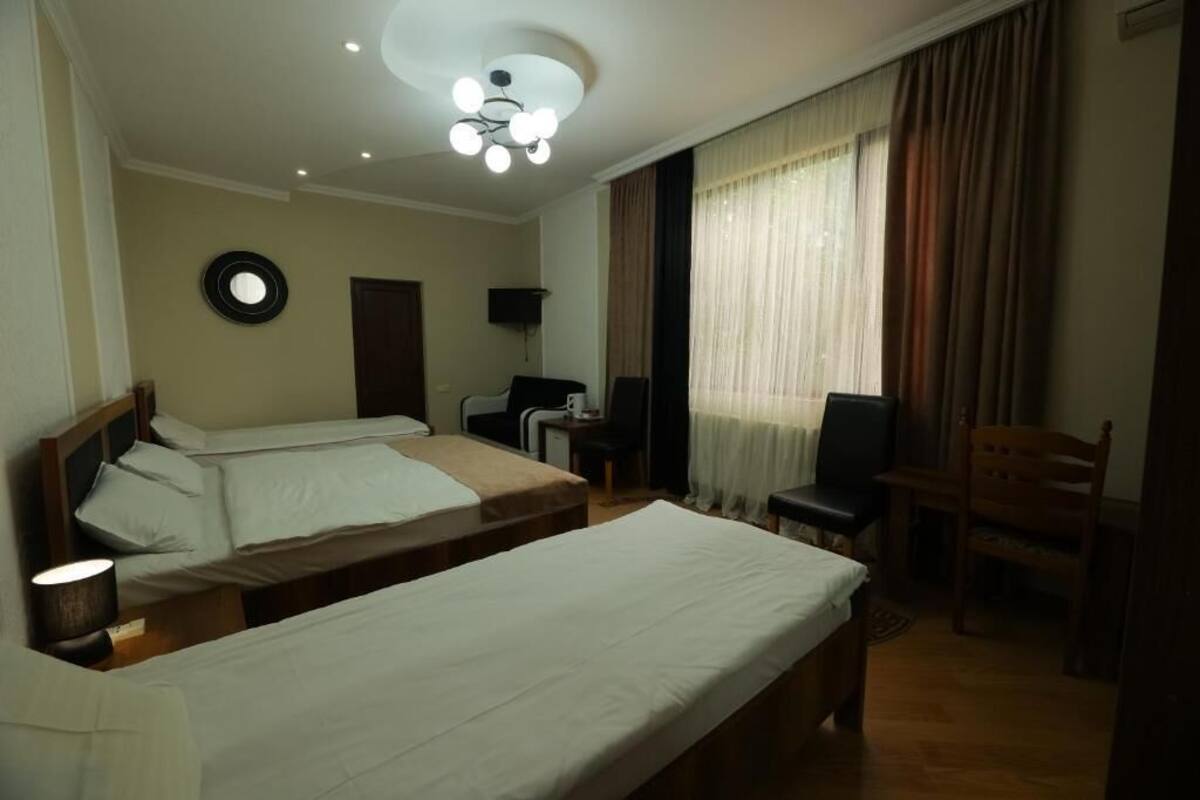 Quarto de hotel com duas camas de solteiro, uma escrivaninha, uma cadeira, uma televisão e um lustre.