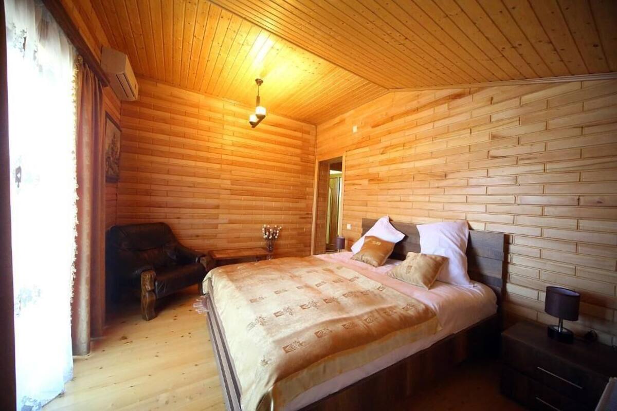 Um quarto com paredes de madeira, uma cama, uma cadeira e uma mesa de cabeceira.