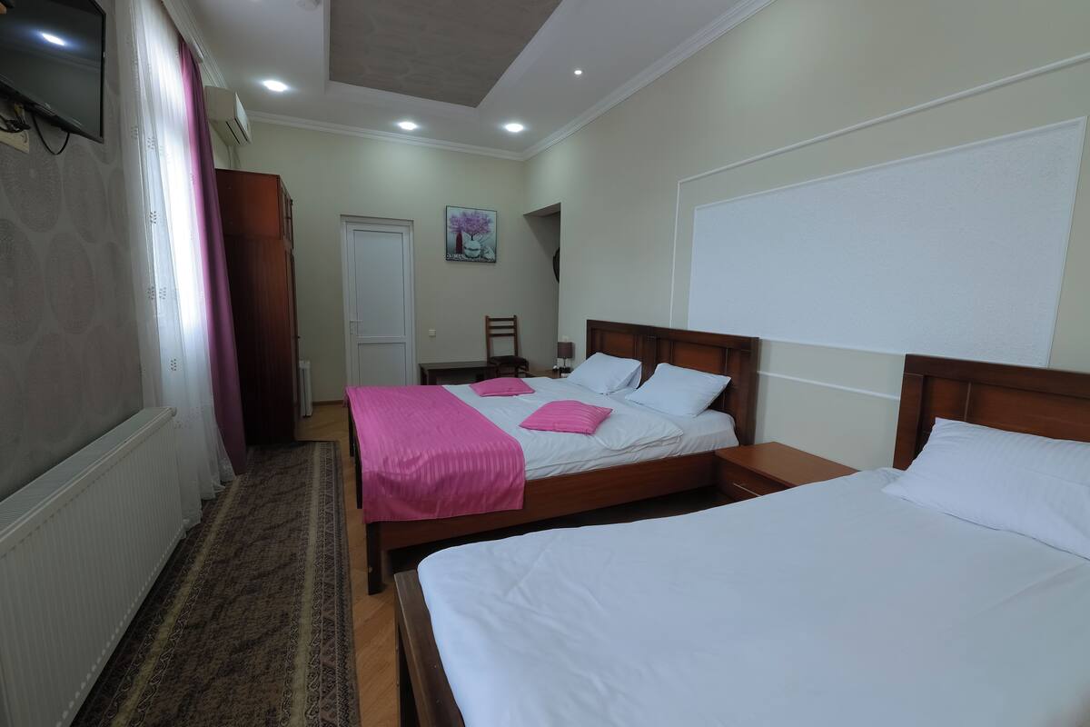 Quarto de hotel com duas camas, televisão, um quadro e guarda-roupa de madeira.