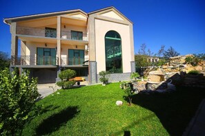 A two-story building with a balcony, a stone wall, and a well-maintained lawn.