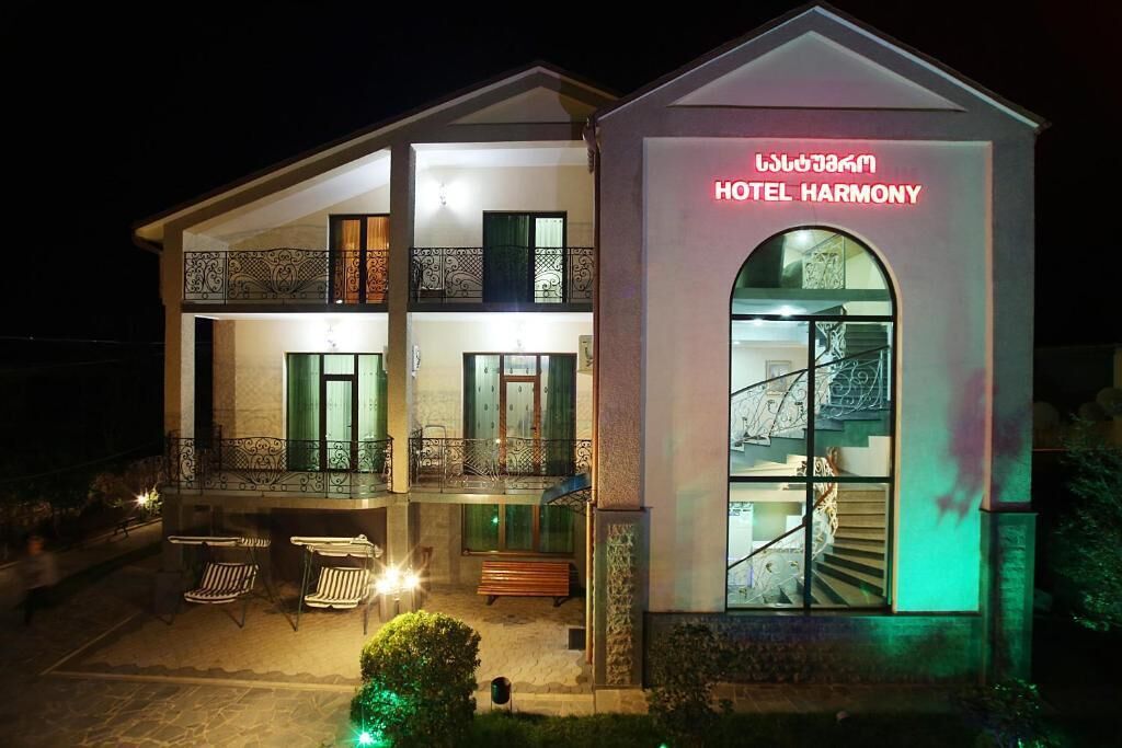 Un hotel de dos pisos con un balcón, mobiliario exterior y una escalera que conduce a la entrada.