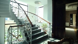 Un magnifique escalier orné de rampes en métal ouvragé et d’une main courante en bois, menant à un palier surmonté d’un lustre.