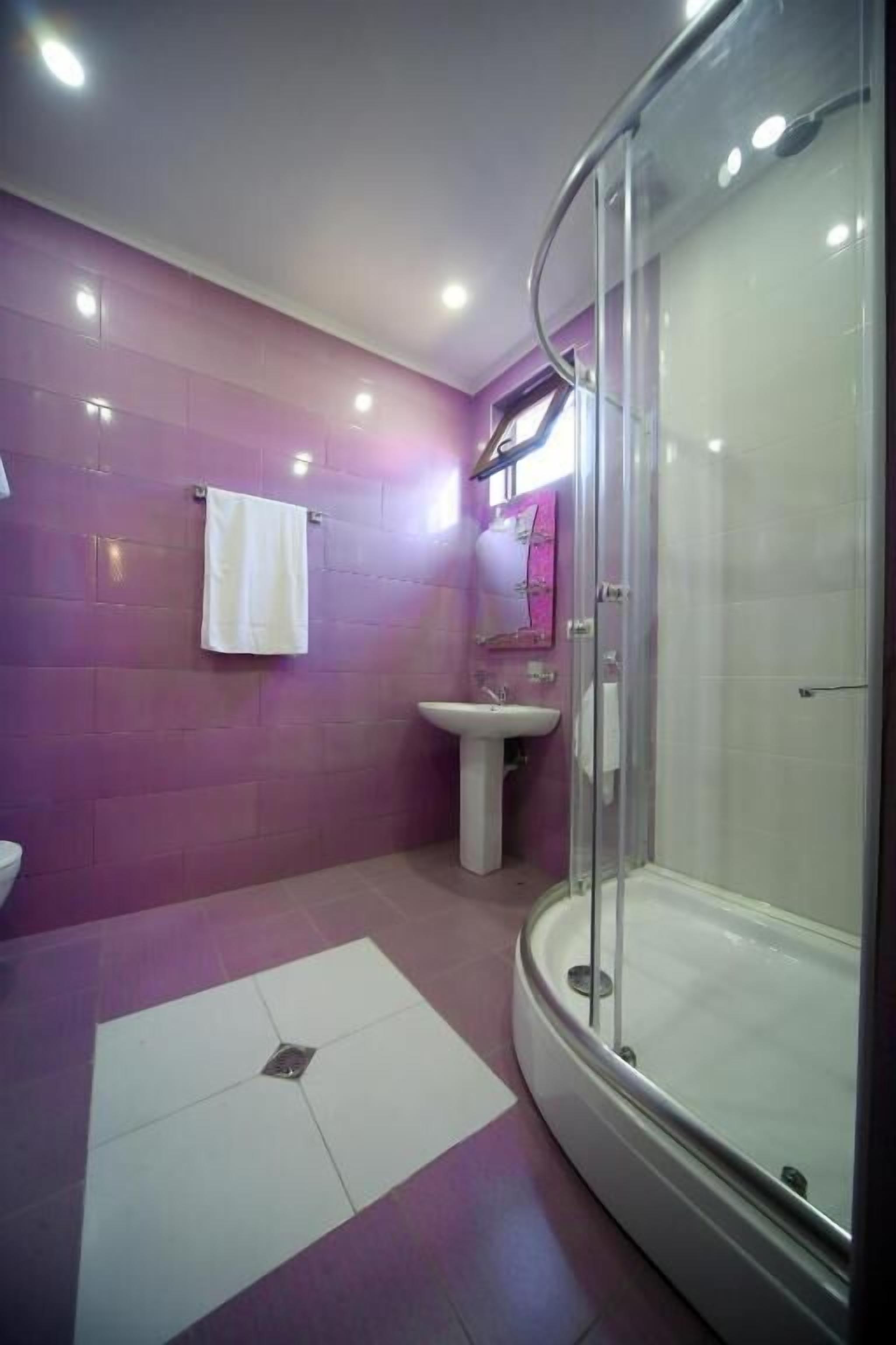 A modern bathroom with a glass shower enclosure, a pedestal sink, and a white towel hanging on the wall.