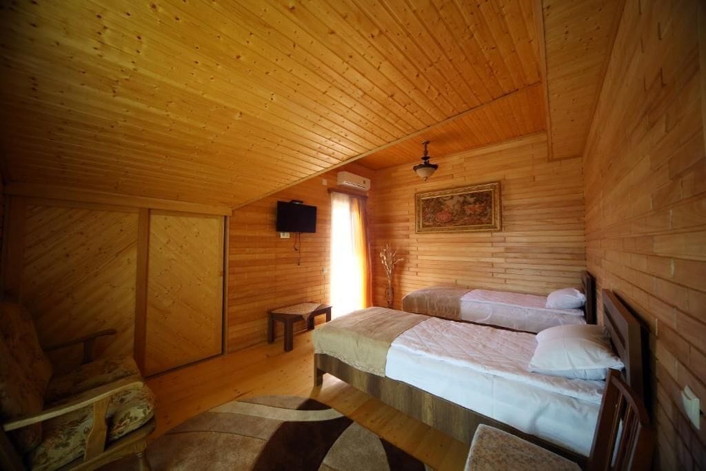 Quarto de cabana de madeira com duas camas, uma televisão e um quadro na parede.