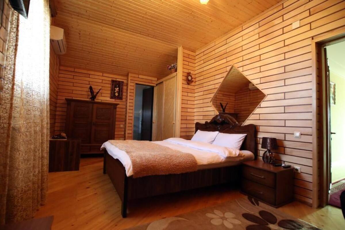 Quarto com painéis de madeira, uma cama, mesa de cabeceira e um espelho decorativo.