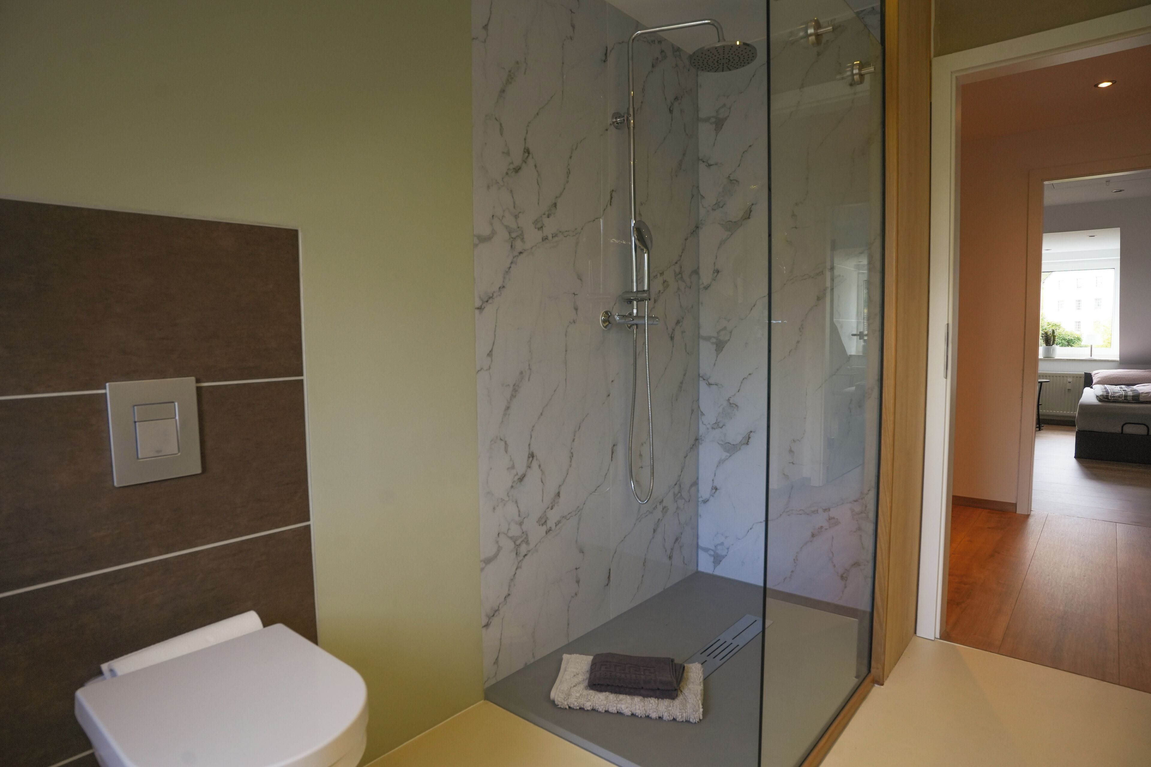Ein Badezimmer mit einer ein Glasfachwerk-Duschkabine, einer weißen Toilette und einer Marmor-Spritzschutzwand.