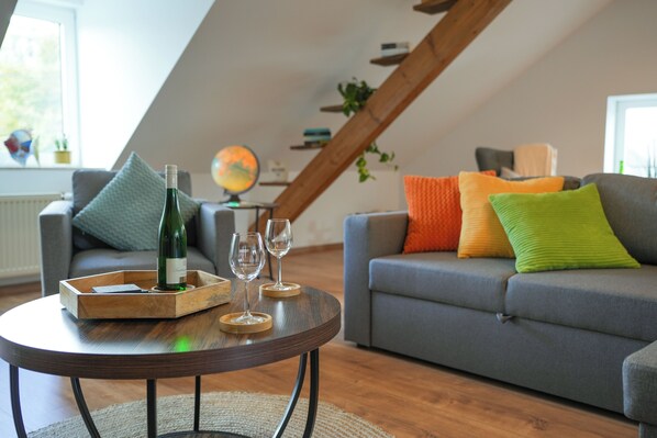 A cozy living room with a round wooden coffee table, a grey sofa with colorful cushions, and a globe on a shelf.