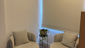 A corner room with two round beige armchairs, a small table with a potted plant, and a window with blinds.