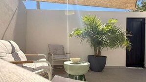 A cozy outdoor seating area with a cushioned sofa, a small round table, and a potted plant. - JOSY Atelier (Ferrel)