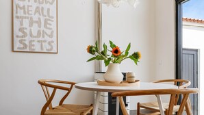 A dining area with a round table, two wooden chairs, a white vase with flowers, and a wall-mounted sign. - JOSY Atelier (Ferrel)