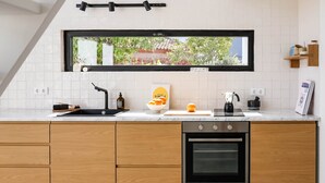 A modern kitchen with wooden cabinets, a built-in oven, a sink, and a window with a view of greenery outside. - JOSY Atelier (Ferrel)