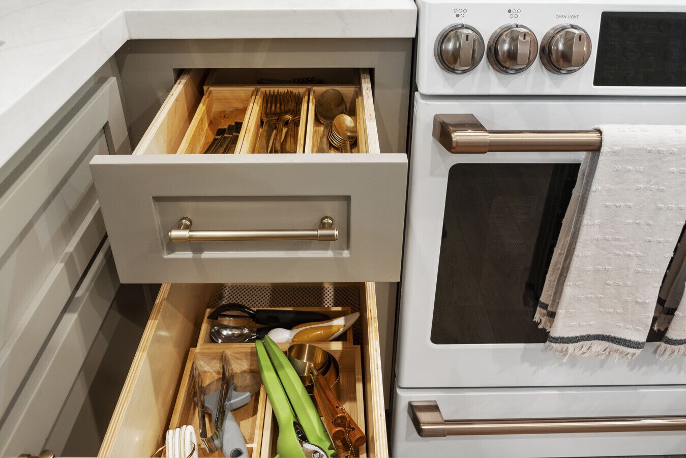 A kitchen drawer with utensils and a stove with oven light controls.